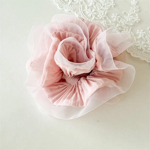 Close-up of the delicate light pink organza fabric and ruffled petal texture of the scrunchie