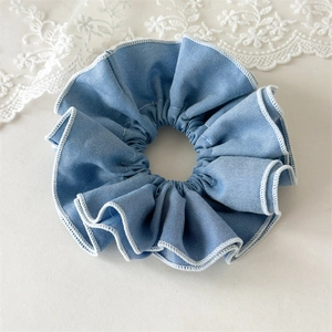 Close-up of denim blue ruffled hair scrunchie with white scalloped edges on lace background