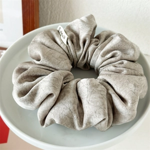 Detail of grey marble texture scrunchie with brand label on a white ceramic tray