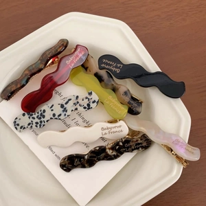 Dettaglio di varie forcine a onde in acetato colorato su un vassoio di ceramica