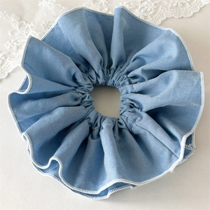 Detail of light blue fabric scrunchie featuring white overlock stitching and soft cotton texture