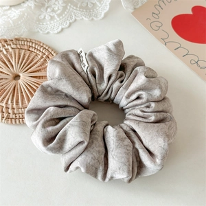 Detail of taupe marble textured hair scrunchie with soft satin finish and woven label