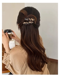 Dettaglio di due fermagli ondulati in acetato tartarugato su capelli castani