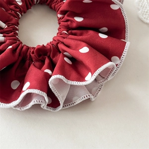 Detail of red polka dot scrunchie featuring white ruffled edges and soft texture
