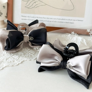 Detail of satin bow hair claw clip with contrast trim and elegant metal logo accent