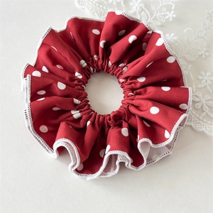 Detail view of red polka dot scrunchie with white scalloped edges and textured fabric