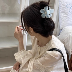 Détail de la pince à cheveux fleur bleu clair avec perle dans une coiffure mi-haute