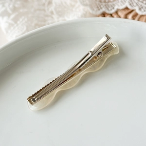 Dettaglio del fermaglio per capelli in acetato ondulato crema su vassoio in ceramica