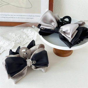 Detail view of large butterfly hair claws with elegant satin bows and metal M logo
