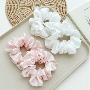 Detailed view of silk satin hair scrunchies in white and pink on an elegant tray