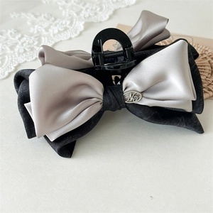 Detail of elegant oversized bow hair claw clip with silver satin and black fabric texture