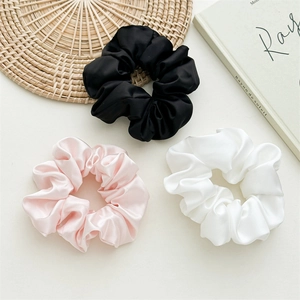 Three elegant satin silk hair scrunchies in black, pink, and white on a natural mat