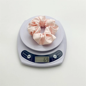 Pink silk-like satin scrunchie weighing 6.9g on a digital scale for lightweight hair styling