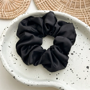 Close-up of black silk satin scrunchie on white tray with elegant pleated texture