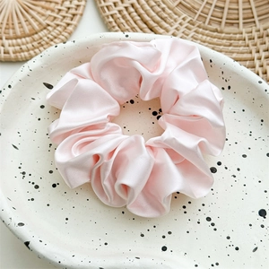 Detailed close-up of light pink satin scrunchie displayed on a ceramic dish