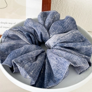 Close-up of elegant blue textured fabric scrunchie on a white plate with aesthetic background