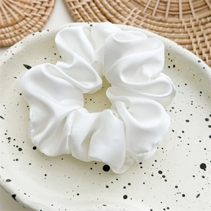 Detail of white satin scrunchie with soft silk texture on a decorative ceramic tray