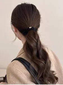Détail d'un chouchou noir avec boucle dorée sur une queue de cheval avec manteau beige