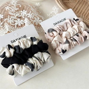 Dettaglio di un set di tre elastici per capelli su cartoncino con sfondo in pizzo delicato