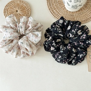Close-up of two large floral chiffon scrunchies with elegant pleats and rustic textures