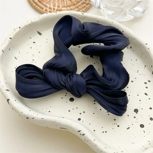 Détail de la texture en satin plissé bleu marine sur un chouchou avec nœud papillon