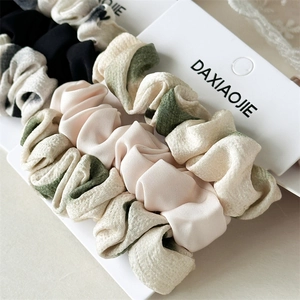 Dettaglio di tre elastici per capelli in raso nei colori nero, beige e fantasia