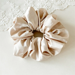 Gros plan sur un chouchou en satin champagne avec texture de soie lisse et plis doux