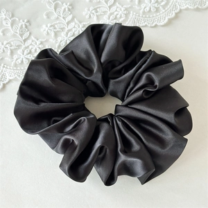 Détail d'un chouchou en satin noir montrant la texture brillante et les plis soyeux du tissu