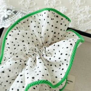 Gros plan du chouchou blanc à pois noirs avec bordure festonnée verte et tissu léger élégant