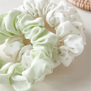 Close-up of mint green satin scrunchie and white polka dot hair tie set with fabric texture