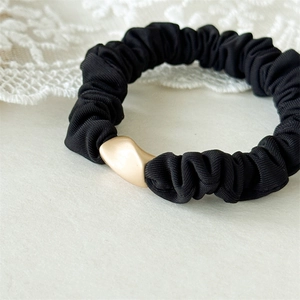 Détail d'un chouchou noir épais doté d'une boucle géométrique en métal doré mat