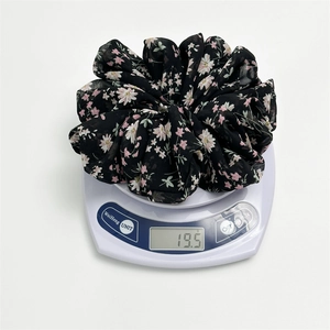 Detail shot of a black chiffon floral scrunchie on a scale weighing 19.5 grams