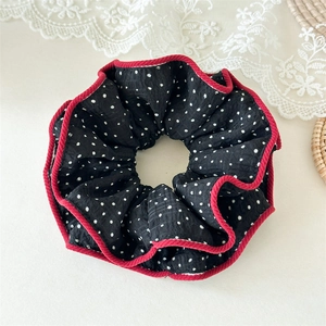 Détail d'un chouchou noir à pois blancs avec bordure rouge et texture de tissu plissé