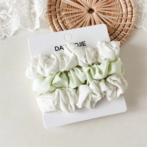 Three-piece set of pale green and polka dot satin scrunchies on white packaging card