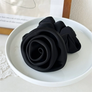Close-up of black satin rose hair scrunchie on a ceramic plate with elegant fabric texture