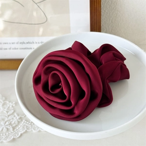 Macro view of a deep red satin rose hair tie on a white ceramic plate with lace detail