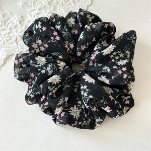Close-up of a large black chiffon floral scrunchie with white and pink daisy patterns