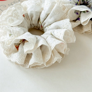 Close-up of floral embroidery on beige linen scrunchie with lace trim and hollow details