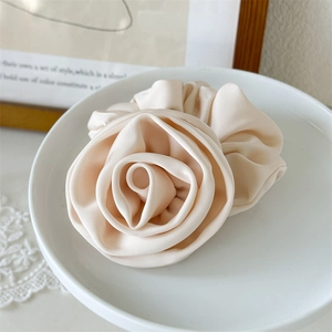 Detailed view of elegant satin rose hair scrunchie in cream color on a porcelain plate