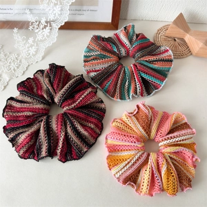 Close-up of three knitted oversized scrunchies in striped patterns on a retro desk