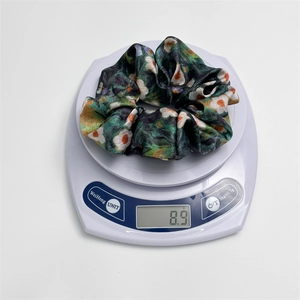 Detailed view of dark green floral satin scrunchie weighing 8.9g on a digital scale