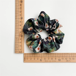 Close-up of green floral satin scrunchie showing 10cm diameter measurement on ruler