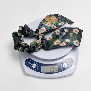 Detail view of a green floral satin ribbon scrunchie weighing only 10.4g on a scale