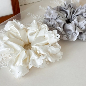 Detail von eleganten Satin-Haargummis in Creme und Grau mit feiner Spitzenumrandung
