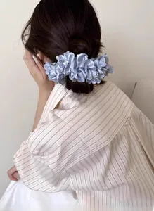 Rückansicht eines hellblauen Satin-Blumen-Scrunchies mit Stickerei an einem Dutt-Haarstyling