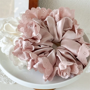 Detail von rosa und elfenbeinfarbenen Satin-Haargummis mit eleganten Lochstickerei-Spitzenkanten
