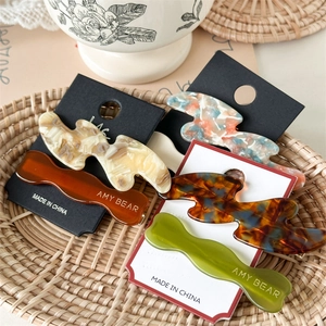 Set of minimalist wavy acetate hair clips in amber and marble textures on a tray