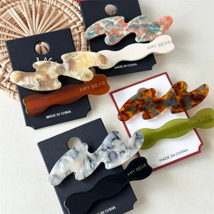 Detailed macro of wavy acetate hair clips showing diverse marble textures and glossy finish