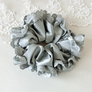 Nahaufnahme von elegantem grauem Satin-Scrunchie mit feinen Ösen-Stickerei-Details