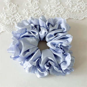 Detailansicht eines hellblauen Satin-Haargummis mit weißer Spitzenbestickung und Blumen